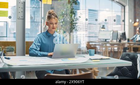 Porträt einer lächelnden weißen Frau, die an einer kreativen Stelle in einer Werbefirma mit Laptop arbeitet. Glücklicher Manager, der mit Kollegen interagiert und einen Marketingplan verfasst Stockfoto