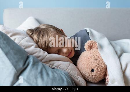 Der Vorschuljunge schläft auf dem Sofa im Wohnzimmer und umarmt seinen Teddybär. Stockfoto