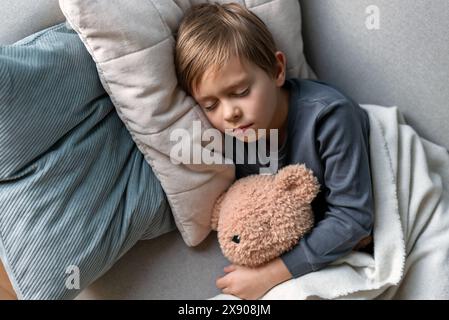 Der Vorschuljunge schläft auf dem Sofa im Wohnzimmer und umarmt seinen Teddybär. Stockfoto