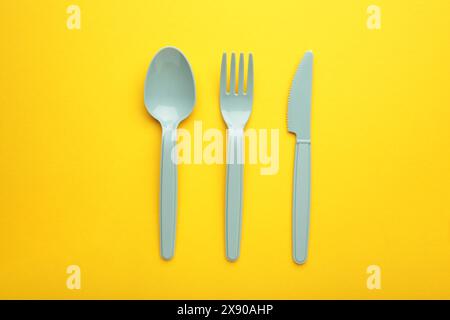 Blaue Plasic Gabeln, Löffel und Messer auf gelbem Hintergrund mit Kopierraum. Stockfoto