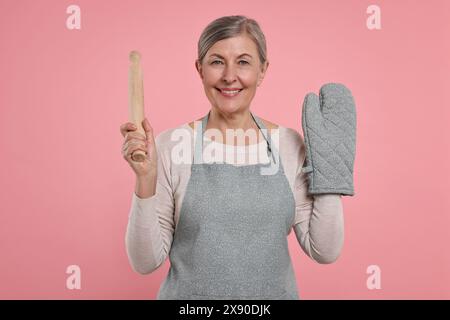 Glückliche Hausfrau mit Ofenhandschuh und Pin auf rosa Hintergrund Stockfoto