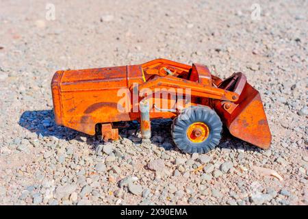 Nahaufnahme eines kleinen, orangen, rostigen Spielzeugbulldozers, isoliert auf einer Kiesoberfläche. Stockfoto