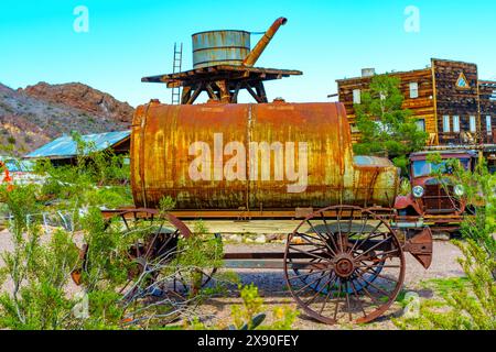 Nelson, Nevada - 15. April 2024: Rostiger, altmodischer Wasserwagen aus Metall, der an einem hölzernen Wasserturm in Nelson Ghost Town angesetzt wird. Stockfoto