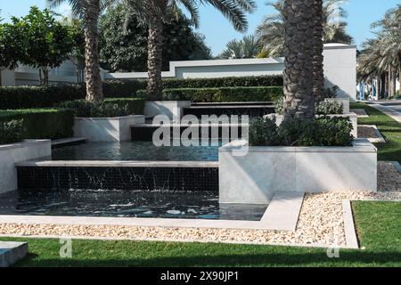 Dubai, VAE - 6. Januar 2024: Modernes Wasserspiel inmitten von üppigem Grün und Palmen in einer ruhigen Stadtlandschaft. Stockfoto