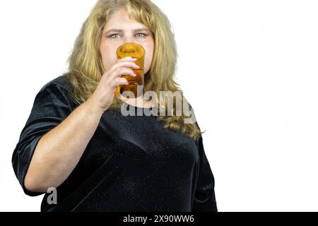 Dieses Bild fängt den ruhigen Moment einer 50-jährigen blonden Frau mit auffälligen grünen Augen ein, die ein erfrischendes Glas Wasser genießt. Stockfoto