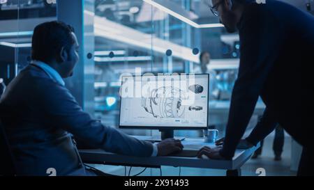 Zwei Industrieingenieure diskutieren über Arbeitsprojekte, sprechen und verwenden Desktop-Computer in der Turbinenfabrik. Spezialisten und Fachleute, die innovative Turbinenmotoren erforschen und entwickeln. Stockfoto