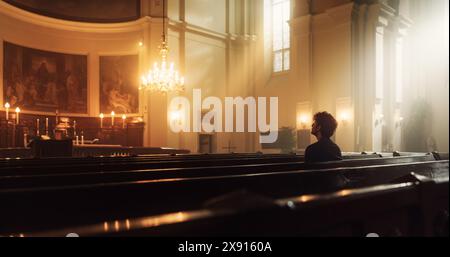 Der junge christliche Mann sitzt frommer in der Majestic Church, mit gefalteten Händen sucht er beim Beten Führung von ihrem religiösen Glauben und ihrer Spiritualität. Christentum und glaube an Macht und Liebe Gottes Stockfoto