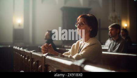 Gruppe treuer Pfarrer in der Großen alten Kirche, die Predigt hören. Die fromme christliche Lady mit gefalteten Händen betet. Die Menschen suchen moralische Führung von der Religios-Fait am heiligen Ort Stockfoto