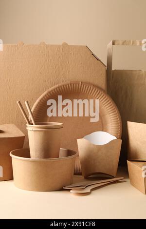 Umweltfreundliche Lebensmittelverpackungen. Papierbehälter, Geschirr und Tasche auf weißem Tisch vor beigefarbenem Hintergrund Stockfoto