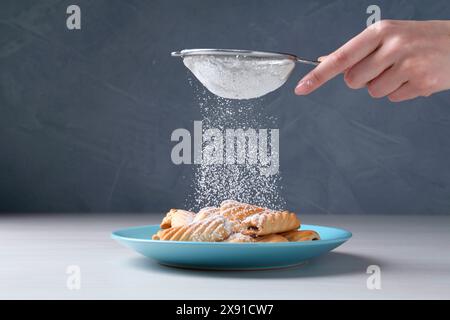 Frau mit einem Sieb, das Puderzucker auf Kekse streut, an weißem Holztisch, Nahaufnahme Stockfoto