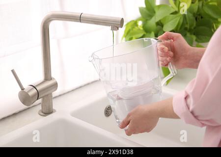 Frau, die Filterkanne mit Wasser aus dem Wasserhahn in der Küche füllt, Nahaufnahme Stockfoto