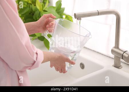 Frau, die Filterkanne mit Wasser aus dem Wasserhahn in der Küche füllt, Nahaufnahme Stockfoto