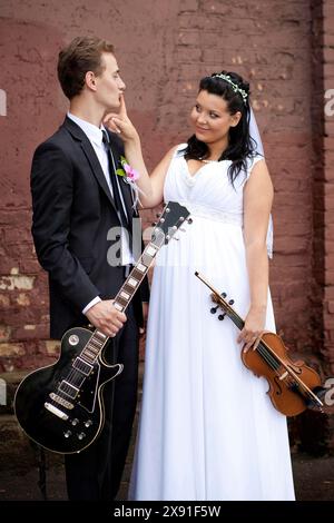 Eine Braut in einem weißen Kleid berührt spielerisch das Gesicht des Bräutigams, während beide Musikinstrumente halten, Weißrussland, Minsk Stockfoto