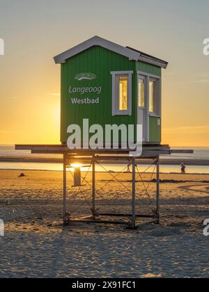 Eine grüne Rettungshütte am Strand, während die Sonne im Hintergrund untergeht, Abendstimmung am Strand mit Sonnenuntergang über dem Meer, Liegen im Strand Stockfoto