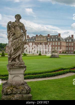 Steinskulptur in einem eleganten Garten mit einem großen Schloss im Hintergrund und wolkigem Himmel, historisches Schloss mit einem grünen Park mit Skulpturen und Stockfoto