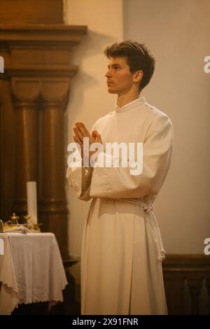 Porträt eines männlichen jungen Ministers in weißen Gewändern, der demütig während der Zeremonie der Heiligsten Kommunion stand. Ein Diener Gottes auf dem Weg der Gerechtigkeit durch den Glauben, dem Christentum gewidmet Stockfoto