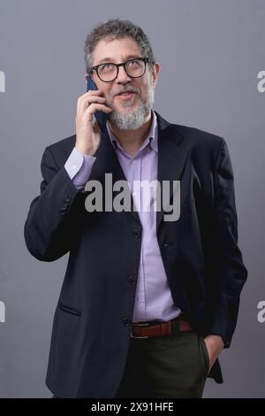 Porträt eines lächelnden Geschäftsmannes, der einen dunklen Anzug und eine Brille trägt und auf einem Mobiltelefon spricht. Dieses Image betont Unternehmenskommunikation, Professionsio Stockfoto