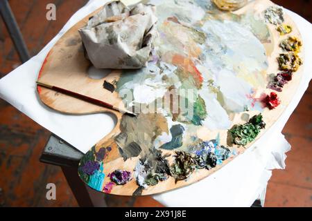 Hölzerne Kunstpalette mit Farb- und Pinselflecken. Hintergrund des kreativen Workshops. Nahansicht Stockfoto