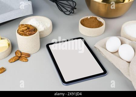 Digitales Touchscreen-Tablet mit Zutaten für Brownie-Rezepte und Küchenutensilien auf grauem Hintergrund, Draufsicht. Stockfoto