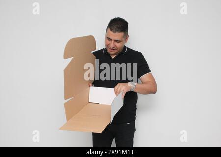 Ein Erwachsener Latino baut einen Karton nach den Anweisungen zusammen, um ihn zu erreichen Stockfoto