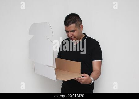 Ein Erwachsener Latino baut einen Karton nach den Anweisungen zusammen, um ihn zu erreichen Stockfoto