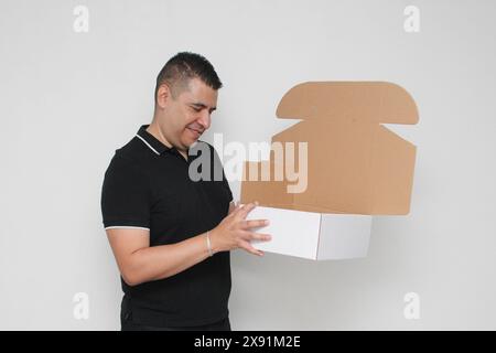 Ein Erwachsener Latino baut einen Karton nach den Anweisungen zusammen, um ihn zu erreichen Stockfoto