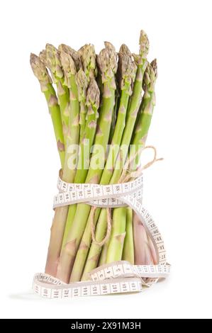 Ein Bündel frischer grüner Spargel ist eng mit einem Maßband umwickelt und symbolisiert gesunde Ernährung und Ernährungsbewusstsein. Das hellgrüne spe Stockfoto