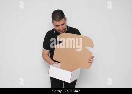 Ein Erwachsener Latino baut einen Karton nach den Anweisungen zusammen, um ihn zu erreichen Stockfoto