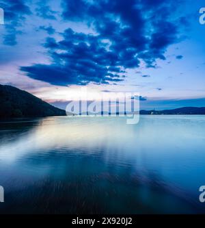 Eine ruhige Abendszene über der Embalse de Puente Nuevo mit leuchtend blauem Himmel und Silhouette der Berge. Stockfoto