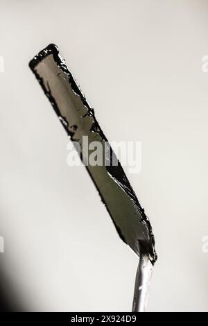Ein detailreiches Nahbild eines in Hochglanz-Schwarz lackierten Palettenmessers, das die Texturen und den Glanz vor einem sanft verschwommenen Hintergrund zeigt. Stockfoto