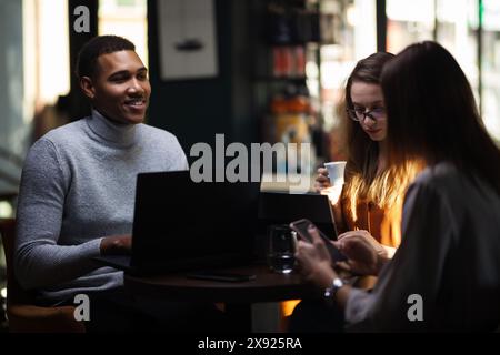 Drei multirassische Geschäftskollegen, die nach der Arbeit oder während einer Kaffeepause in einem Restaurant ein Meeting abhalten. Freunde, die in einer Café-Bar arbeiten. Stockfoto