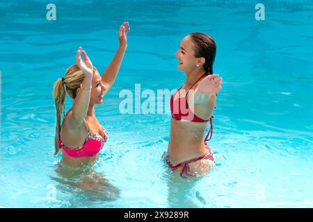 2 junge Frauen springen mit Freunden von Angesicht zu Angesicht im Wasser, während sie die Arme schwingen Aquagym-Session 016644 137 Stockfoto