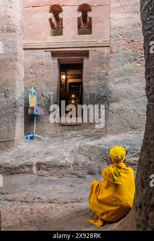 Ältere Frau pilgert in Gelb am Eingang der felsengehauenen monolithischen ortodoxen Kirche von Bete Medhane Alem, Lalibela, Region Amhara, Äthiopien. Stockfoto