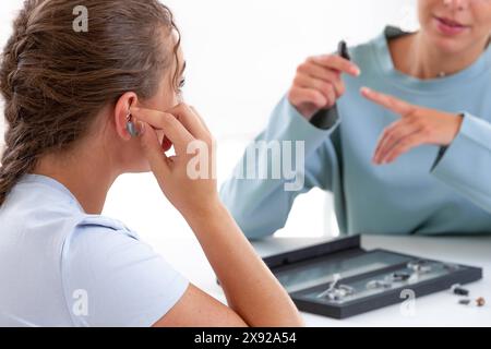 Frau vor einem Hörgeräteakustiker, der ein Hörgerät testet. Hörprobleme bei einer jungen Frau 016644 051 Stockfoto