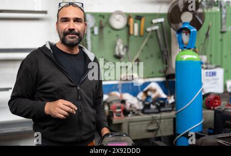 Porträt eines Schmieds während einer Schweißpause. Er nutzt die Gelegenheit, eine Zigarette zu rauchen, der Helm des Schweißers ist im bo zu sehen Stockfoto