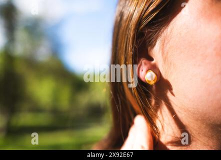 Eine junge Frau trägt einen goldenen und perlenförmigen Ohrring, der an ihrem rechten Ohr in einer natürlichen Umgebung im Freien getragen wird Stockfoto