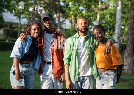 Zwei verliebte afroamerikanische Studentenpaare stehen während des Spazierens im Park und blicken lächelnd in die Kamera. Stockfoto
