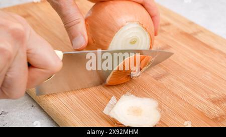 Schälen und Schneiden von weißen Zwiebeln auf einem Schneidebrett. Gemüsesuppen-Rezept. Zutaten aus der Nähe auf dem Küchentisch Stockfoto