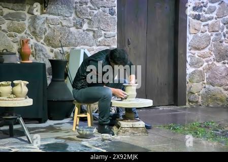 Konzentrierter Handwerker, der Ton auf einem Keramikrad in einer rustikalen Werkstatt mit Steinwänden und Erdtöpfen in der Nähe formt Stockfoto