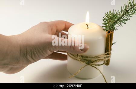 Eine Kerze in der Hand einer Frau, eine Kerze mit einem Tannenzweig und einem Zimtstab. Stockfoto