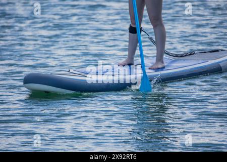 Nahaufnahme der Beine einer jungen Frau auf einem Paddleboard, während sie an einem sonnigen Sommertag über einen See paddelt und Wassersport im Freien und Freizeit-Spa genießt Stockfoto