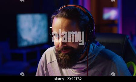 E-Sports-Spieler, der während des Livestreams vor den Abonnenten Videospiele spielt, konzentriert sich darauf, Feinde zu besiegen. Nahaufnahme des fröhlichen Streaming-Spiels für Profi-Gamer mit Kopfhörern Stockfoto