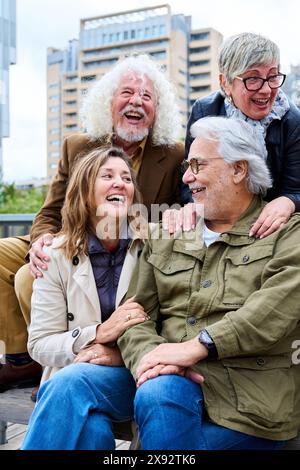 Eine Gruppe älterer kaukasischer Freunde, die Spaß haben, zusammen zu lachen und auf der Bank in der Stadt sitzen. Stockfoto