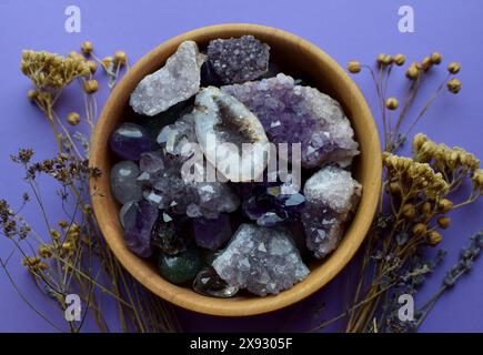 Schöne Drusch- und Amethyst-Kristalle auf einem Holzteller und trockene Kräuter auf einem lila Hintergrund. Vorhersagen, Hexerei, spirituelle esoterische Praxis. Stockfoto