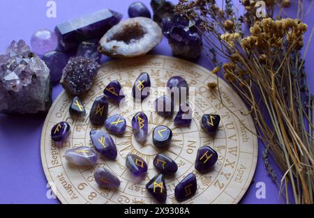 Amethyst-Kristalle, skandinavische Runen und trockene Kräuter auf einem violetten Hintergrund mit einem Brett mit Symbolen der Tierkreiszeichen. Vorhersagen, Hexerei, spi Stockfoto