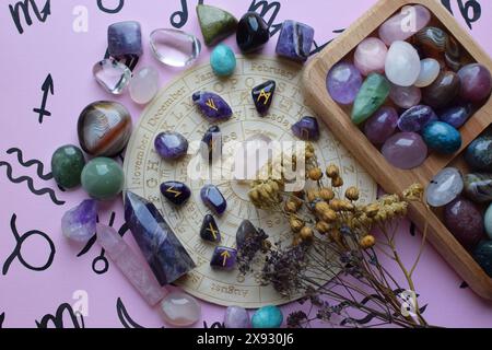 Skandinavische Runen aus Amethyst und trockenen Kräutern auf rosa Hintergrund mit einem Brett mit Symbolen der Tierkreiszeichen. Vorhersagen, Hexerei, Spiritus Stockfoto