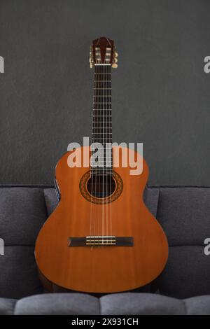 Kreolische Gitarre, die auf einem grauen Sofa steht, mit einer grauen Wand auf dem Hintergrund Stockfoto