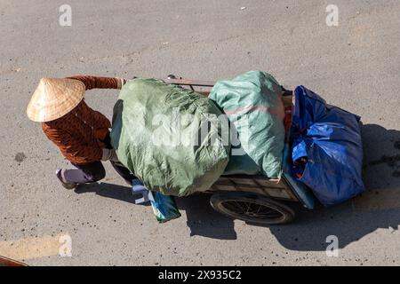 Sammlung von recycelbaren Abfällen in den Straßen von Ho Chi Minh. Vietnamesische Frau schiebt einen Wagen voller Taschen, Saigon City. Stockfoto