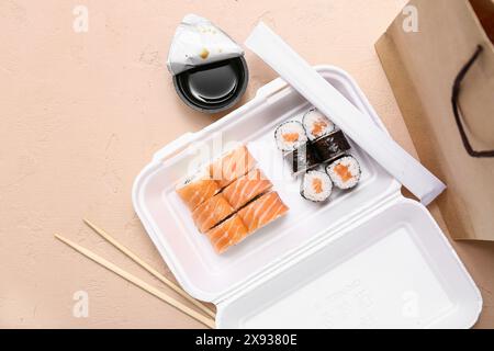 Plastikbehälter mit leckeren Sushi-Rollen, Essstäbchen und Papiertüte auf beigem Grunge-Hintergrund. Lieferkonzept Stockfoto