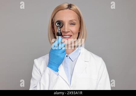 Glücklicher Dermatologe mit Dermatoskop auf grauem Hintergrund Stockfoto